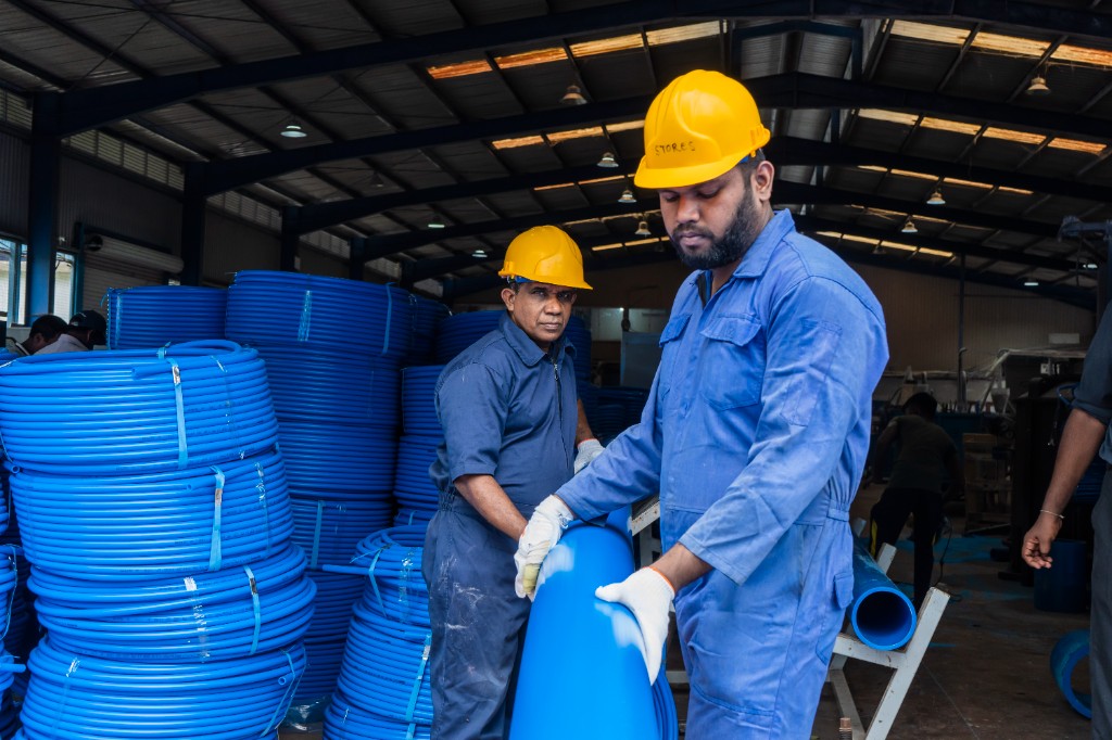 Workers handling large blue pipes in the manufacturing facility